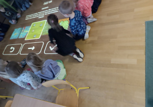 Dzieci siedzące dookoła magicznego dywanu (interaktywna zabwka, która wyświetla na podłodzę gry dla dzieci)