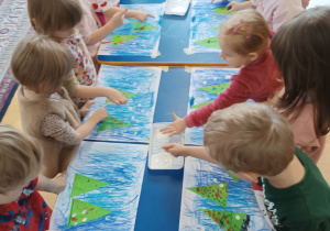 Dzieci stemplują palcem umoczonym w białej farbie.